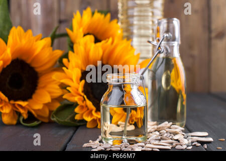 Dodsolnechnoe Öl in eine Flasche mit einem großen und einem kleinen, ein Blumenstrauß aus Sonnenblumen Blumen, auf einem winzigen Hintergrund und verstreuten Samen. Natürliches Produkt, rustikalen Stil. Platz kopieren Stockfoto