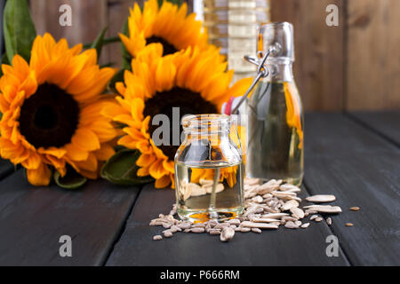 Dodsolnechnoe Öl in eine Flasche mit einem großen und einem kleinen, ein Blumenstrauß aus Sonnenblumen Blumen, auf einem winzigen Hintergrund und verstreuten Samen. Natürliches Produkt, rustikalen Stil. Platz kopieren Stockfoto