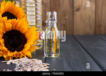 Dodsolnechnoe Öl in eine Flasche mit einem großen und einem kleinen, ein Blumenstrauß aus Sonnenblumen Blumen, auf einem winzigen Hintergrund und verstreuten Samen. Natürliches Produkt, rustikalen Stil. Platz kopieren Stockfoto