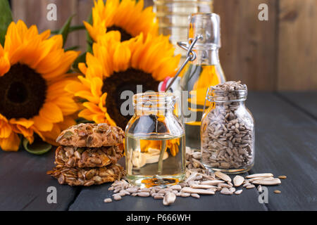 Dodsolnechnoe Öl in eine Flasche mit einem großen und einem kleinen, ein Blumenstrauß aus Sonnenblumen Blumen, auf einem deryl Hintergrund. Kekse mit Samen. Natürliches Produkt, rustikalen Stil. Platz kopieren Stockfoto