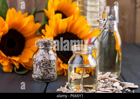 Dodsolnechnoe Öl in eine Flasche mit einem großen und einem kleinen, ein Blumenstrauß aus Sonnenblumen Blumen, auf einem winzigen Hintergrund und verstreuten Samen. Natürliches Produkt, rustikalen Stil. Platz kopieren Stockfoto