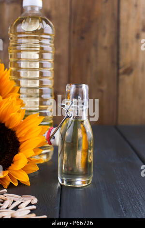 Dodsolnechnoe Öl in eine Flasche mit einem großen und einem kleinen, ein Blumenstrauß aus Sonnenblumen Blumen, auf einem winzigen Hintergrund und verstreuten Samen. Natürliches Produkt, rustikalen Stil. Platz kopieren Stockfoto