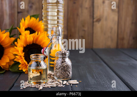 Dodsolnechnoe Öl in eine Flasche mit einem großen und einem kleinen, ein Blumenstrauß aus Sonnenblumen Blumen, auf einem winzigen Hintergrund und verstreuten Samen. Natürliches Produkt, rustikalen Stil. Platz kopieren Stockfoto