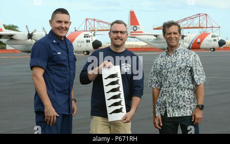 Cmdr. Jeffrey Jager, Operations Officer für Coast Guard Air Station Friseure, Eric Roberts, Marine Mammal Antwort Koordinator für die Küstenwache 14. Bezirk und David Schofield, nationalen ozeanischen und atmosphärischen Leitung Marine Mammal Gesundheit und Response Program Manager, posieren mit sieben Hawaiian monk seal Aufkleber auf einer HC-130 Hercules Flugzeug in Air Station Friseure, Oahu, 16. Mai 2016 gestellt werden. NOAA stellte die Hawaiianische Mönchsrobbe Abziehbilder Air Station Herrenfriseure Punkt Crew in Anerkennung ihrer wesentlichen Beitrag zur hawaiianischen Mönchsrobbe Erhaltung Programm. (U Stockfoto