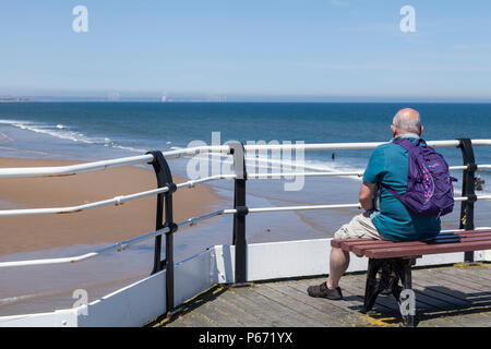 Älterer Mann saß auf einer Bank am Pier mit Blick aufs Meer in Saltburn am Meer, England, Großbritannien Stockfoto