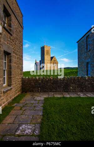 St Helena die Kirche durch zwei Ferienhäuser auf Lundy Island gerahmt Stockfoto