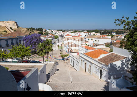 Häuser der historischen Stadt Castro Marim. Platz mit verschiedenen Bäumen. Auf der linken Seite Befestigung der mittelalterlichen Burg. Strahlend blauen Himmel. Castro Marim Stockfoto