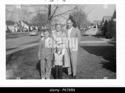 Schwarz-weiß Foto, zeigt eine Familie, in der vollen Länge, zusammen Posieren im Freien, der Mann mittleren Alters, mit einem zurücktretenhaarstrich, trägt einen hellen Anzug und steht mit einem kurzhaarigen Frau, trug einen Rock, Bluse und Handschuhe, und zwei Jungen, beide trugen Anzüge, die Kleinere trägt eine zweifarbige Jacke, mit Bäumen, Oldtimer und s-Häuser im Hintergrund sichtbar, wahrscheinlich in Ohio, Juni, 1956 fotografiert. () Stockfoto