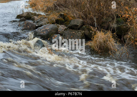 Herbst turbulenten Fluss fließen und Felsbrocken mit Laub am Ufer des Flusses Stockfoto