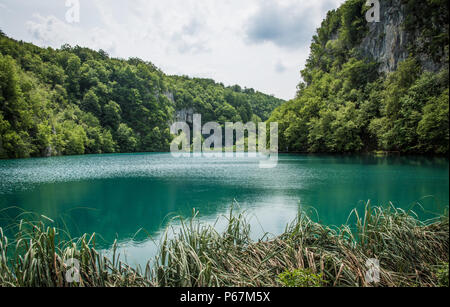 Atemberaubende Aussicht auf einem der vielen schönen Seen Plitvicer Nationalpark an einem warmen Sommertag, von üppigen Klippen umgeben. Eine idyllische Reiseziel! Stockfoto