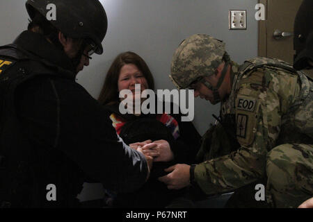 New York Army National Guard Staff Sgt. Blake Alexander Mitglied der 1108Th EOD Firma Komfort "Katie" ein "Opfer" für ein Training wie er entfernt eine Bombe aus ihrem Hals als Teil der Ausbildung darf 18 an der New York State Vorbereitung Training Center in Corato New York, als lokale Sheriff Deputy an schaut. New York Armee Nationalgarde für eine Woche neben nationalen und internationalen EOD Militär- und Gesetzdurchführungpersonal während einer Übung namens Raven's Challenge, Mai 16-20 ausgebildet. (U.S. Army National Guard Foto von Sgt. J.p. Lawrence/freigegeben). Stockfoto