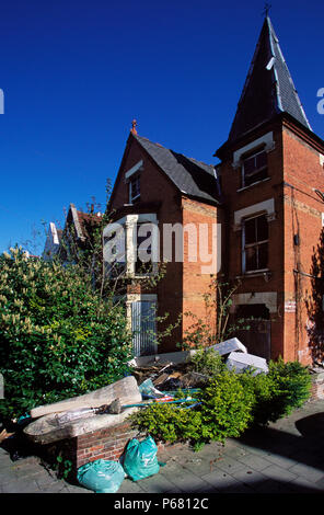 Müll im Vordergrund der Garten mit Brettern vernagelt Haus. Süd-London, Vereinigtes Königreich. Stockfoto