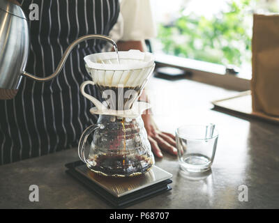 Barista die Zubereitung von Filterkaffee, Hand gießen heißes Wasser aus dem Wasserkocher über das Kaffeepulver. Stockfoto