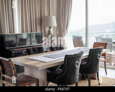 Moderner Luxus Esszimmer mit Esstisch aus Holz, Luxus Stühle auf dem Teppich, klassisches Klavier, Tischleuchte und den Vorhang in der Nähe der Terrasse O Stockfoto