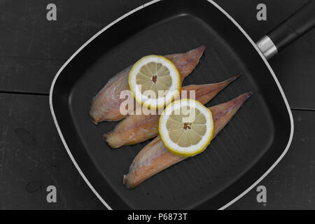 Geräucherte Makrele Fischfilets mit Zitrone in einer Bratpfanne Pfanne zum Kochen mit schwarzem Holz Hintergrund vorbereitet Stockfoto