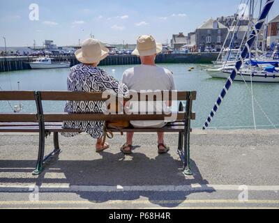 Padstow Cornwall UK 29. Juli 2018. Menschen die Sonne sitzen auf einer Bank mit Blick auf den Hafen an einem schönen Sommertag genießen. Temperaturen erreicht die Hohe 20 von centigrade als das Wetter weiter. Kredit Julian Eales/Alamy leben Nachrichten Stockfoto