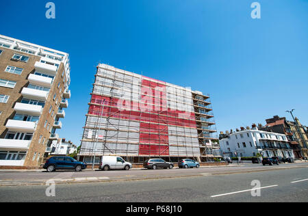 Hove Brighton, UK. 29 Juni, 2018. Ein riesiger England St Georges Cross Flag wurde umgesetzt, indem Gerüstbauer auf einem Wohnblock in St Catherines Terrasse entlang der Strandpromenade Hoves entfernt in der Nähe von Brighton. Die 120 ft 60 ft-Flag hat durch die Jahreszeiten Gerüst zur Unterstützung von England bei der WM 2018 in Russland mit der nächsten Runde Spiel gegen Kolumbien Anfang nächster Woche: Simon Dack/Alamy Leben Nachrichten gehalten werden gesetzt worden Stockfoto