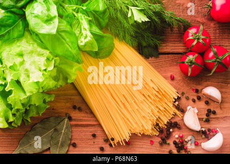 Italienische Pasta Spaghetti mit Kirschtomaten, frisch grüne Basilikum, Salat und Gewürzen - Ansicht von oben auf Holz Hintergrund Stockfoto