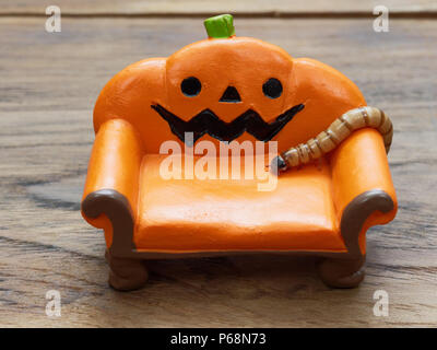 Super oder riesigen Wurm kriecht auf orange Miniatur Keramik Kürbis Couch oder Sofa über dunklen Holz- Oberfläche mit Kopie Raum als Hintergrund in Halloween, Ornament, Feier, und Dekoration Stockfoto