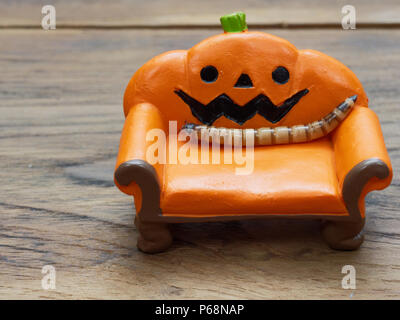 Super oder riesigen Wurm kriecht auf orange Miniatur Keramik Kürbis Couch oder Sofa über dunklen Holz- Oberfläche mit Kopie Raum als Hintergrund in Halloween, Ornament, Feier, und Dekoration Stockfoto