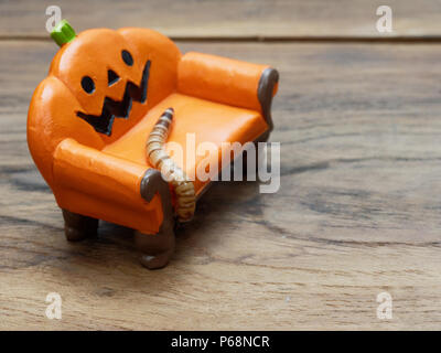 Super oder riesigen Wurm kriecht auf orange Miniatur Keramik Kürbis Couch oder Sofa über dunklen Holz- Oberfläche mit Kopie Raum als Hintergrund in Halloween, Ornament, Feier, und Dekoration Stockfoto