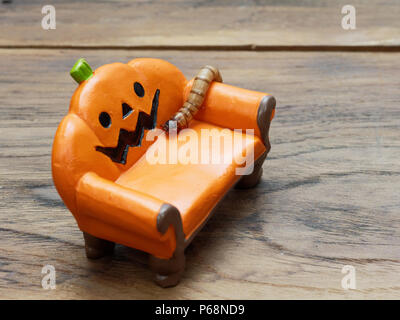 Super oder riesigen Wurm kriecht auf orange Miniatur Keramik Kürbis Couch oder Sofa über dunklen Holz- Oberfläche mit Kopie Raum als Hintergrund in Halloween, Ornament, Feier, und Dekoration Stockfoto