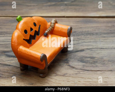 Super oder riesigen Wurm kriecht auf orange Miniatur Keramik Kürbis Couch oder Sofa über dunklen Holz- Oberfläche mit Kopie Raum als Hintergrund in Halloween, Ornament, Feier, und Dekoration Stockfoto