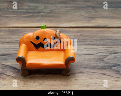 Super oder riesigen Wurm kriecht auf orange Miniatur Keramik Kürbis Couch oder Sofa über dunklen Holz- Oberfläche mit Kopie Raum als Hintergrund in Halloween, Ornament, Feier, und Dekoration Stockfoto