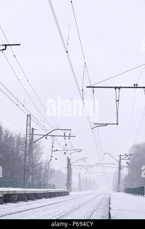 Eisenbahn Landschaft in der kalten Jahreszeit. Schneebedeckten Bahnhof Plattform und Neblig bewölkten Himmel bei starkem Schneefall Stockfoto