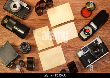 Vintage Kamera, Fotografie Zubehör und leeren Bilderrahmen auf hölzernen Tisch. Stillleben mit kopieren. Ansicht von oben. Retro getonten Bild in beige Farbe Stockfoto