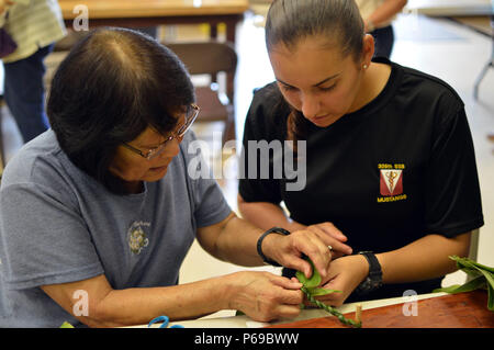 Linda Hirano (links), ein wahiawa Rainbow Senioren Freiwillige, zeigt Pfc. Vanessa Sheika, zu der 325 Brigade Support Bataillon zugeordnet, 3. Brigade Combat Team, 25 Infanterie Division, wie Lei aus einem Ti Leaf am Wahiawa District Park, Colorado, am 27. Mai 2016 zu machen. Wahiawa Rainbow Senioren und 3 BCT Soldaten produziert fast 1.900 auf die grabsteine an der Schofield Barracks Post Friedhof am Memorial Day platziert werden. (U.S. Armee Foto: Staff Sgt. Armando R. Limon, 3. Brigade Combat Team, 25 Infanterie Division). Stockfoto