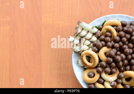 Knusprige Tubuli, Schokolade schmelzen Kugeln und Bagels liegen in einer weißen Platte auf einem Holztisch. Mix aus verschiedenen Süßigkeiten. Stockfoto