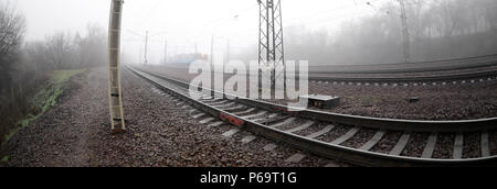 Die Ukrainische s-bahn eilt entlang der Bahnstrecke in einem nebligen Morgen. Fisheye Foto mit erhöhter Verzerrung. Stockfoto