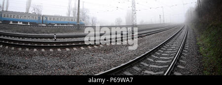 Die Ukrainische s-bahn eilt entlang der Bahnstrecke in einem nebligen Morgen. Fisheye Foto mit erhöhter Verzerrung. Stockfoto