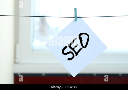 SEO. Hinweis befindet sich auf einem weißen Aufkleber, die mit einer Wäscheklammer an einem Seil auf einem Hintergrund von Fensterglas hängt geschrieben. Stockfoto