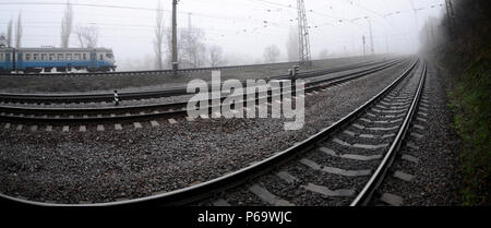 Die Ukrainische s-bahn eilt entlang der Bahnstrecke in einem nebligen Morgen. Fisheye Foto mit erhöhter Verzerrung. Stockfoto