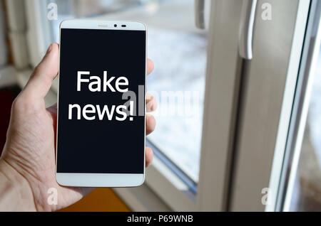 Ein Mensch sieht, ein weißer Aufschrift auf einem BlackBerry-Smartphone angezeigt werden, den er in seiner Hand hält. Gefälschte Nachrichten! . Stockfoto