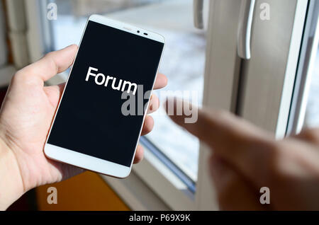 Ein Mensch sieht, ein weißer Aufschrift auf einem BlackBerry-Smartphone angezeigt werden, den er in seiner Hand hält. Forum. Stockfoto