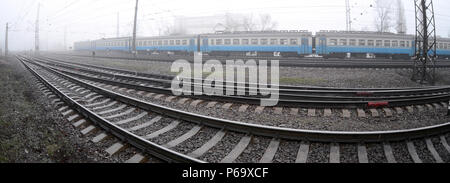 Die Ukrainische s-bahn eilt entlang der Bahnstrecke in einem nebligen Morgen. Fisheye Foto mit erhöhter Verzerrung. Stockfoto