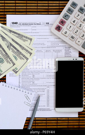 Zusammensetzung der Elemente liegen auf dem 1040 Steuerformular. Dollarscheine, Kugelschreiber, Taschenrechner, Smartphone, Büroklammer und Notepad. Die Zeit, die Steuern zu bezahlen. Stockfoto