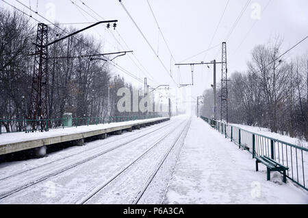 Eisenbahn Landschaft in der kalten Jahreszeit. Schneebedeckten Bahnhof Plattform und Neblig bewölkten Himmel bei starkem Schneefall Stockfoto