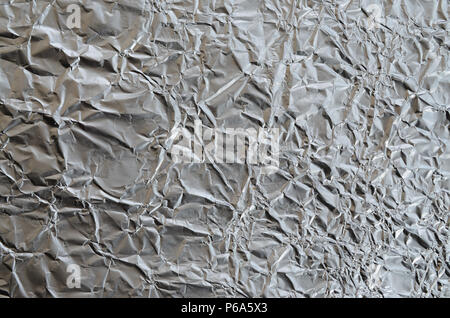 Dünne zerknittertes Blatt zerdrückt Zinn Aluminium silber Folie Hintergrund mit glänzenden zerknitterten Oberfläche für Textur. Stockfoto