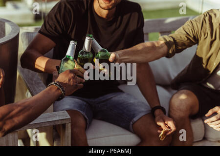 Schließen Sie bis zu drei Freunde ihre Flaschen Bier toasten, während eine Party im Freien. Männer, die ihre Flaschen für einen Toast. Stockfoto