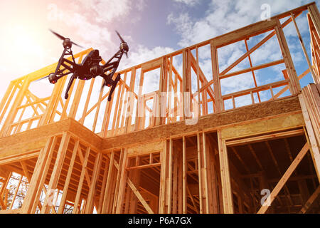 Schwarz drone quadcopter mit Kamera fliegt über Wohnungsbau home Framing vor blauem Himmel. Dach- konstruktion. Holzkonstruktion Stockfoto