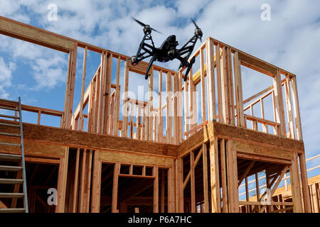 Schwarz drone quadcopter mit Kamera fliegt über Wohnungsbau home Framing gegen das Haus ist neu in Holz Überdachung Stockfoto