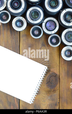 Einige fotografische Objektive und weiße Notebook liegen auf einem braunen Holz- Hintergrund. Platz für Text. Stockfoto