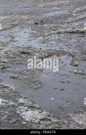 Beschädigte asphaltierte Straße mit Schlaglöchern durch Gefrieren und Auftauen im Winter. Schlechte Straßen. Stockfoto