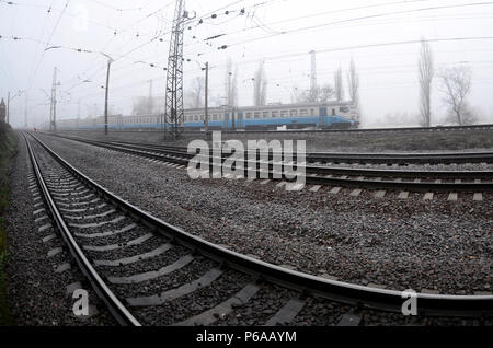 Die Ukrainische s-bahn eilt entlang der Bahnstrecke in einem nebligen Morgen. Fisheye Foto mit erhöhter Verzerrung. Stockfoto