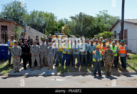 Laredo, Strafverfolger, fünftes Sortierer, Gemeindeleiter und Texas Nationalgarde posieren für ein Gruppenfoto, während ein Texas Army National Guard Soldat demoliert ein Haus in Laredo, Texas, 4. Mai 2016. Die Texas National Guard gemeinsame Counterdrug Taskforce abgerissen etwa 27 Strukturen in Laredo, die von Drogenkonsumenten und Händlern verwendet wurden, als Teil der Task force Betrieb Durchgreifen. (U.S. Air National Guard Foto von 1 Lt Alicia Lacy/Freigegeben) Stockfoto