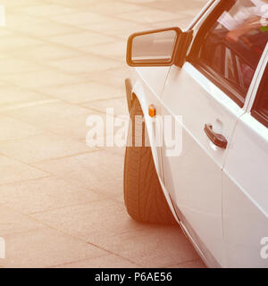 Diagonale Ansicht einer weiß-glänzend Auto, die auf einem Quadrat von grauen Fliesen steht. Stockfoto